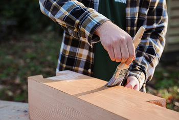 Person oiling a wooden surface outdoors.
