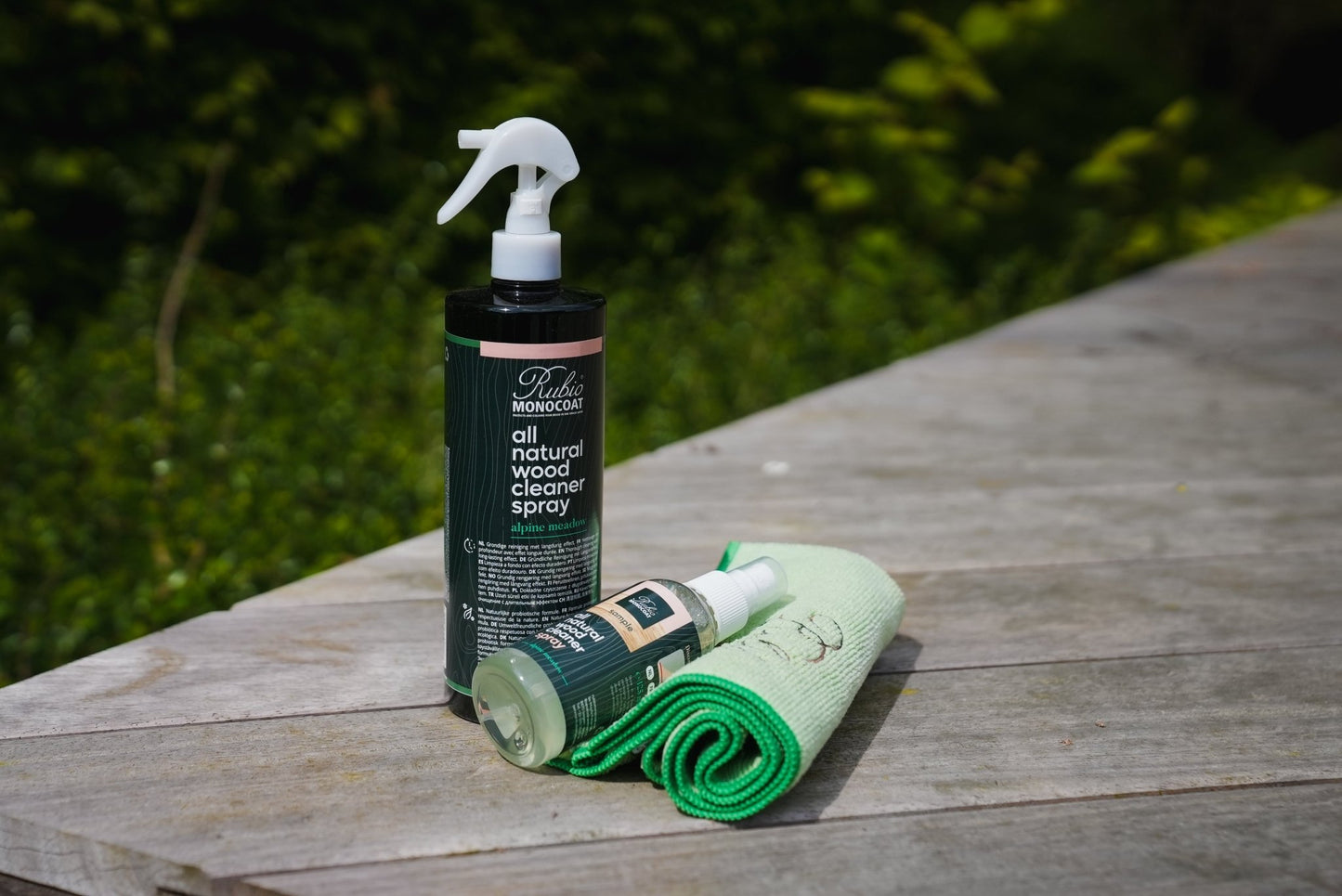 Two bottles of Rubio Monocoat All Naturel Wood Cleaner a wooden surface with a green background.